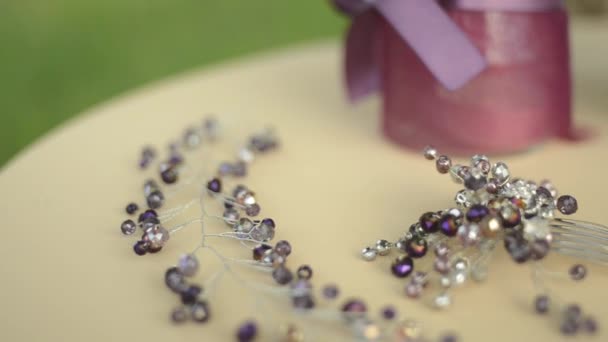 Accesorios de boda en la mesa. Flores púrpuras, tela beige, broche o peine en el cabello para la novia. Enfoque variable, primer plano . — Vídeos de Stock