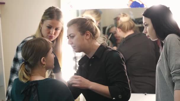 Maquillaje artista, estudiante y modelo. El proceso de aprendizaje. Rubia joven. El maquillador dibujando cejas a una chica guapa con un cepillo profesional delante de un espejo en un salón de belleza . — Vídeo de stock