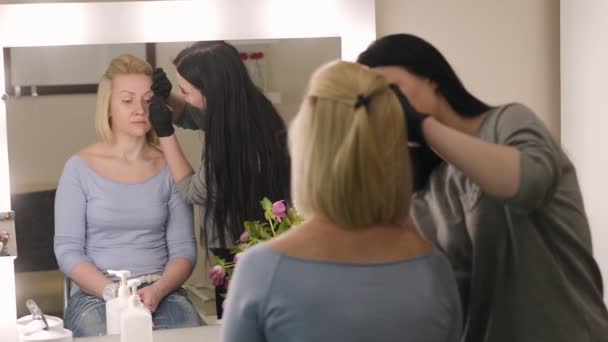 Maquillaje artista y modelo. Jovencita. El maquillador dibujando cejas a una chica guapa con un cepillo profesional delante de un espejo en un salón de belleza . — Vídeos de Stock
