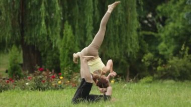 Güzel çift Acro yoga uygulamak. Yeşil çimenlerin üzerinde bir şehir parkta genç yoga eğitmenleri pratik. İki başarılı gençler acro yoga egzersizleri yapın. Erkek ve kadın gün batımında yoga öğrenmek.