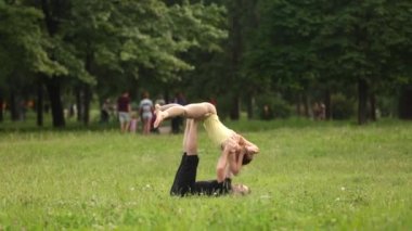 Güzel çift Acro yoga uygulamak. Yeşil çimenlerin üzerinde bir şehir parkta genç yoga eğitmenleri pratik. İki başarılı gençler acro yoga egzersizleri yapın. Erkek ve kadın gün batımında yoga öğrenmek.