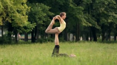 Güzel çift Acro yoga uygulamak. Yeşil çimenlerin üzerinde bir şehir parkta genç yoga eğitmenleri pratik. İki başarılı gençler acro yoga egzersizleri yapın. Erkek ve kadın gün batımında yoga öğrenmek.