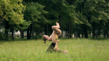 Güzel çift Acro yoga uygulamak. Yeşil çimenlerin üzerinde bir şehir parkta genç yoga eğitmenleri pratik. İki başarılı gençler acro yoga egzersizleri yapın. Erkek ve kadın gün batımında yoga öğrenmek.