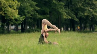 Güzel çift Acro yoga uygulamak. Yeşil çimenlerin üzerinde bir şehir parkta genç yoga eğitmenleri pratik. İki başarılı gençler acro yoga egzersizleri yapın. Erkek ve kadın gün batımında yoga öğrenmek.
