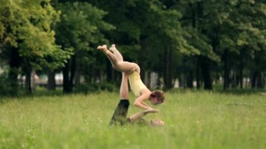 Güzel çift Acro yoga uygulamak. Yeşil çimenlerin üzerinde bir şehir parkta genç yoga eğitmenleri pratik. İki başarılı gençler acro yoga egzersizleri yapın. Erkek ve kadın gün batımında yoga öğrenmek.
