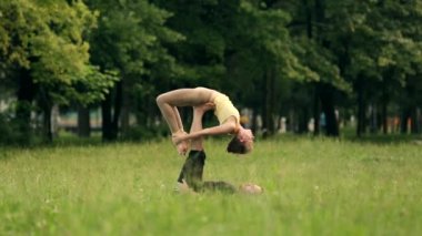 Güzel çift Acro yoga uygulamak. Yeşil çimenlerin üzerinde bir şehir parkta genç yoga eğitmenleri pratik. İki başarılı gençler acro yoga egzersizleri yapın. Erkek ve kadın gün batımında yoga öğrenmek.