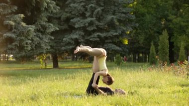 Güzel çift Acro yoga uygulamak. Yeşil çimenlerin üzerinde bir şehir parkta genç yoga eğitmenleri pratik. İki başarılı gençler acro yoga egzersizleri yapın. Erkek ve kadın gün batımında yoga öğrenmek.