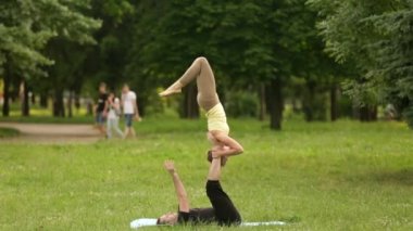 Güzel çift Acro yoga uygulamak. Yeşil çimenlerin üzerinde bir şehir parkta genç yoga eğitmenleri pratik. İki başarılı gençler acro yoga egzersizleri yapın. Erkek ve kadın gün batımında yoga öğrenmek.
