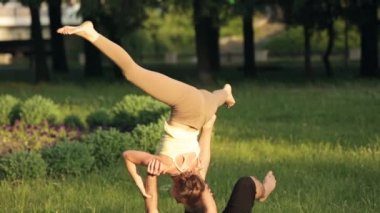 Şaşırtıcı kaç Acro yoga uygulamak. Profesyonel yoga eğitmenleri pratik bir şehir parkı. İki başarılı gençler acro yoga egzersizleri yapın. Erkek ve kadın gün batımında yoga öğrenmek.