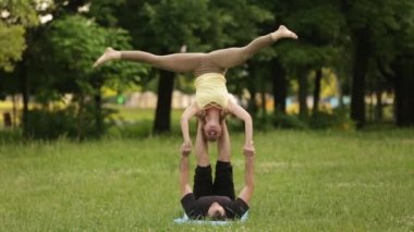 Güzel çift Acro yoga uygulamak. Yeşil çimenlerin üzerinde bir şehir parkta genç yoga eğitmenleri pratik. İki başarılı gençler acro yoga egzersizleri yapın. Erkek ve kadın gün batımında yoga öğrenmek.