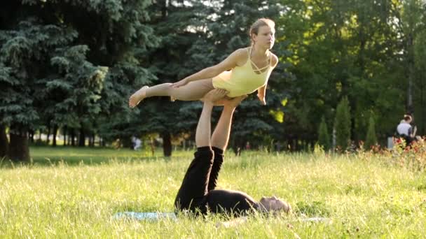 Güzel çift Acro yoga uygulamak. Yeşil çimenlerin üzerinde bir şehir parkta genç yoga eğitmenleri pratik. İki başarılı gençler acro yoga egzersizleri yapın. Erkek ve kadın gün batımında yoga öğrenmek. — Stok video