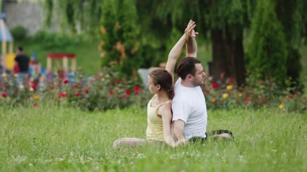 Мужчина и женщина растягиваются перед упражнениями. Молодые инструкторы йоги практикуют в городском парке на зеленой траве. Успешная молодежь выполняет упражнения по акро-йоге . — стоковое видео