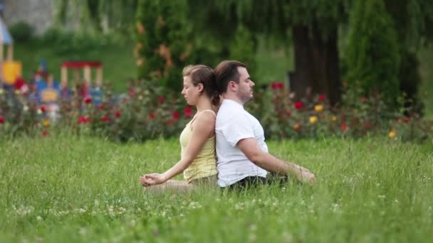 People stretching before doing exercises. Young yoga instructors practice in a city park on green grass. Successful caucasian man and woman taking a rest. — Stock Video