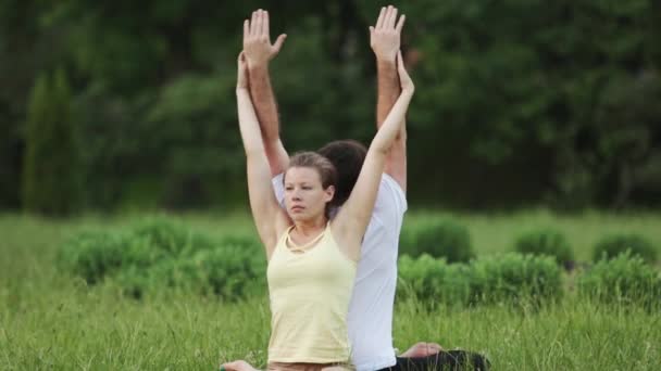 En man och en kvinna som stretching innan du gör övningarna. Unga yoga instruktörer praxis i en park på grönt gräs. Framgångsrika ungdomar utföra acro yogaövningar. — Stockvideo