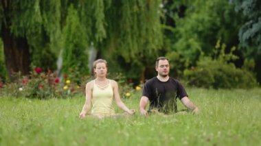 Bir erkek ve bir kadın mutluluk meditasyon. Yeşil çimenlerin üzerinde bir şehir parkta genç yoga eğitmenleri pratik. Başarılı gençlerin acro yoga egzersizleri gerçekleştirmek.