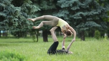 Güzel çift Acro yoga uygulamak. Yeşil çimenlerin üzerinde bir şehir parkta genç yoga eğitmenleri pratik. İki başarılı gençler acro yoga egzersizleri yapın. Erkek ve kadın gün batımında yoga öğrenmek.