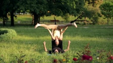 Şaşırtıcı kaç Acro yoga uygulamak. Profesyonel yoga eğitmenleri pratik bir şehir parkı. İki başarılı gençler acro yoga egzersizleri yapın. Erkek ve kadın gün batımında yoga öğrenmek.