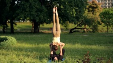 Şaşırtıcı kaç Acro yoga uygulamak. Profesyonel yoga eğitmenleri pratik bir şehir parkı. İki başarılı gençler acro yoga egzersizleri yapın. Erkek ve kadın gün batımında yoga öğrenmek.