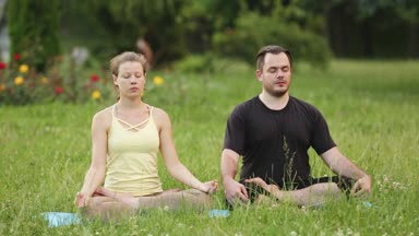 Bir erkek ve bir kadın mutluluk meditasyon. Yeşil çimenlerin üzerinde bir şehir parkta genç yoga eğitmenleri pratik. Başarılı gençlerin acro yoga egzersizleri gerçekleştirmek.