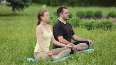Bir erkek ve bir kadın mutluluk meditasyon. Yeşil çimenlerin üzerinde bir şehir parkta genç yoga eğitmenleri pratik. Başarılı gençlerin acro yoga egzersizleri gerçekleştirmek.