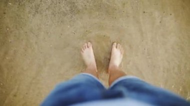 Ayaklarınızı yıkadım okyanus dalgaları tarafından mans ve onları kuma gömer. Mavi Jeans beyaz adam onun ayaklarını yerden su fırçalar ve denize girer. Yakın çekim deniz ya da okyanus kıyısında erkek bacak.