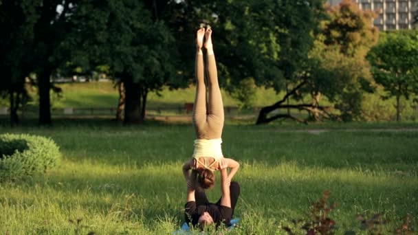 Increíble pareja practicando acro yoga. Los instructores de yoga profesionales practican en un parque de la ciudad. Dos jóvenes exitosos realizan ejercicios de acro yoga. Hombre y una mujer aprenden yoga al atardecer . — Vídeos de Stock