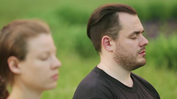 Un hombre y una mujer meditan en la dicha. Jóvenes instructores de yoga practican en un parque de la ciudad sobre hierba verde. Jóvenes exitosos realizan ejercicios de acro yoga . — Vídeos de Stock