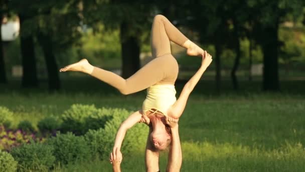 Amazing couple practicing acro yoga. Professional yoga instructors practice in a city park. Two successful young people perform acro yoga exercises. Man and a woman learn yoga at sunset. — Stock Video