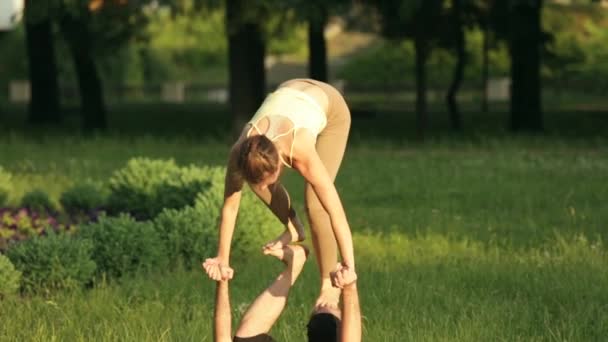 Fantastiska par öva acro yoga. Professionell yoga instruktörer praxis i en stadspark. Två framgångsrika unga människor utföra acro yogaövningar. Man och en kvinna lär dig yoga i solnedgången. — Stockvideo