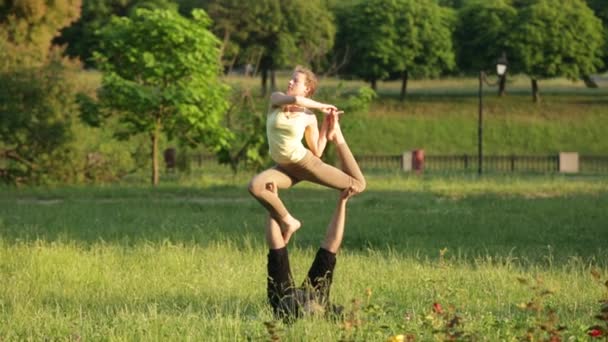 Удивительная пара, практикующая акро-йогу. Профессиональные инструкторы йоги практикуют в городском парке. Два успешных молодых человека выполняют упражнения по акро-йоге. Мужчина и женщина учатся йоге на закате . — стоковое видео