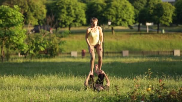 Casal incrível praticando acro ioga. Instrutores de ioga profissionais praticam em um parque da cidade. Dois jovens bem sucedidos realizam exercícios de acro ioga. Homem e uma mulher aprendem ioga ao pôr do sol . — Vídeo de Stock