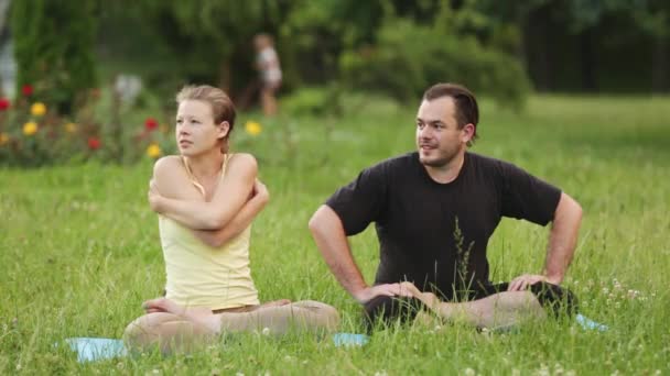Mężczyzna i kobieta odpoczynku i uśmiechał się po medytacji. Acro praktyki instruktorów jogi w parku miejskim na zielonej trawie. — Wideo stockowe