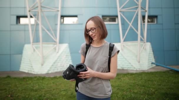 Ragazza sorridente con i capelli corti in possesso di occhiali di realtà virtuale su uno sfondo blu la sera. Tecnologia della realtà virtuale. Concetto VR del futuro . — Video Stock