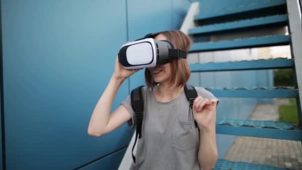 Будущее сейчас. Молодая женщина на лестнице играет в игру или смотрит кино в VR-очках. Молодая белая женщина прикасается к чему-то с помощью современных очков виртуальной реальности на синем фоне . — стоковое видео