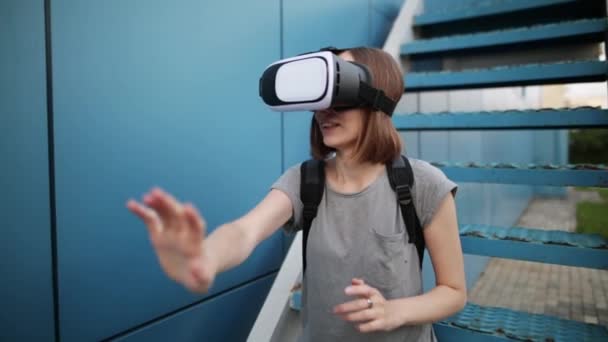 L'avenir est maintenant. Belle jeune femme sur un escalier jouant au jeu dans des lunettes vr. Jeune femme caucasienne toucher quelque chose en utilisant des lunettes de réalité virtuelle moderne sur un fond bleu . — Video