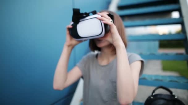 L'avenir est maintenant. Belle jeune femme dans un escalier jouant à un jeu ou regardant un film en lunettes vr. Jeune femme caucasienne toucher quelque chose en utilisant des lunettes de réalité virtuelle moderne sur un fond bleu . — Video