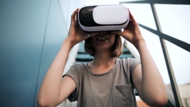 Closeup of girl with a small hands holding virtual reality glasses on a blue background in the evening and taking virtual reality expirience. Female wearing futuristic VR box headset. — Stock Video