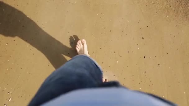 Garvade manliga fötterna på sandstranden vid havet, högt upp Visa. Mannen bär jeans gå barfota på stranden med vatten som täcker fötterna. Sommar och koppla av koncept. — Stockvideo