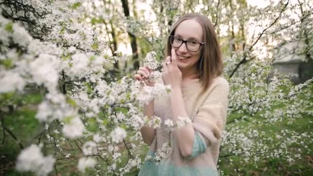 Chica bonita está sonriendo y posando para la cámara en un floreciente parque de primavera . — Vídeo de stock