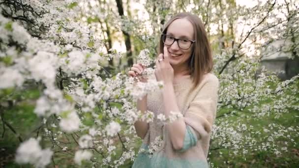 Jolie fille sourit et pose pour la caméra dans un parc printanier en fleurs . — Video