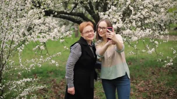 Vezető anya és lány felnőtt lánya figyelembe selfie a virágzó kert. — Stock videók