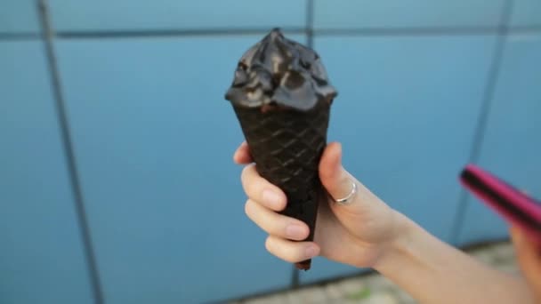 Helado de carbón negro en una mano femenina sobre un fondo azul . — Vídeos de Stock