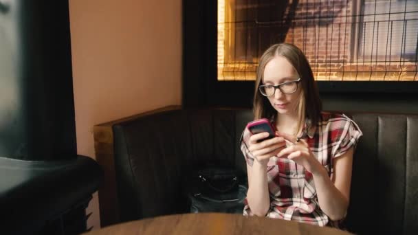 Trendy lächelndes Mädchen mit Brille, das in sozialen Netzwerken plaudert oder etwas liest. — Stockvideo