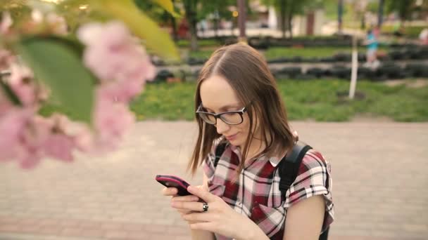 Lycklig kvinna med en telefon i en blommande våren trädgård på kvällen. — Stockvideo