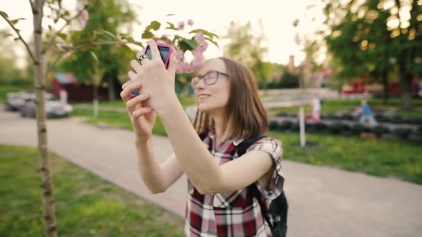 Young attractive woman in glasses taking selfie with sakura flowers.
