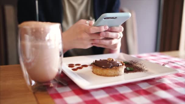 Gadis tampan menulis pesan teks, mengobrol dengan pacarnya menggunakan smartphone duduk di kafe dengan hidangan penutup . — Stok Video