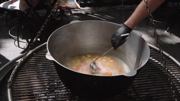 Chef mezcla sopa de mariscos y verduras en un caldero grande en la calle, de cerca. Movimiento lento . — Vídeo de stock