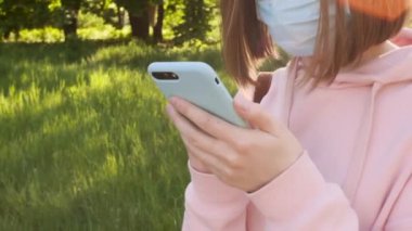 Koruyucu tıbbi maskeli genç bir kız akıllı telefon mesajı kullanıyor. Haber salgını, kendini izole etme.. 