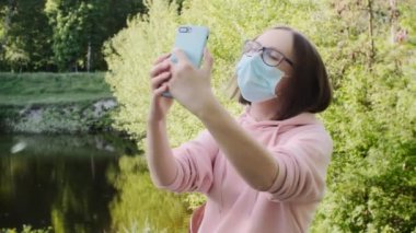 Koruyucu tıbbi maskeli ve gözlüklü genç bir kız akıllı telefondan selfie çekiyor..