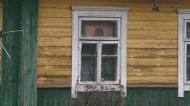 02.13.2019 Opsa Belaus. Bahçeli eski yeşil köy evi. Gri kazlar köy avlusunda otluyor. Metal bir örgüden bak. Evcil hayvanlar 4k.Yıpranmış bir pencerede ışık yanıyor. Evin penceresinde insanların siluetleri görülebiliyor. Yakın plan. 4k.